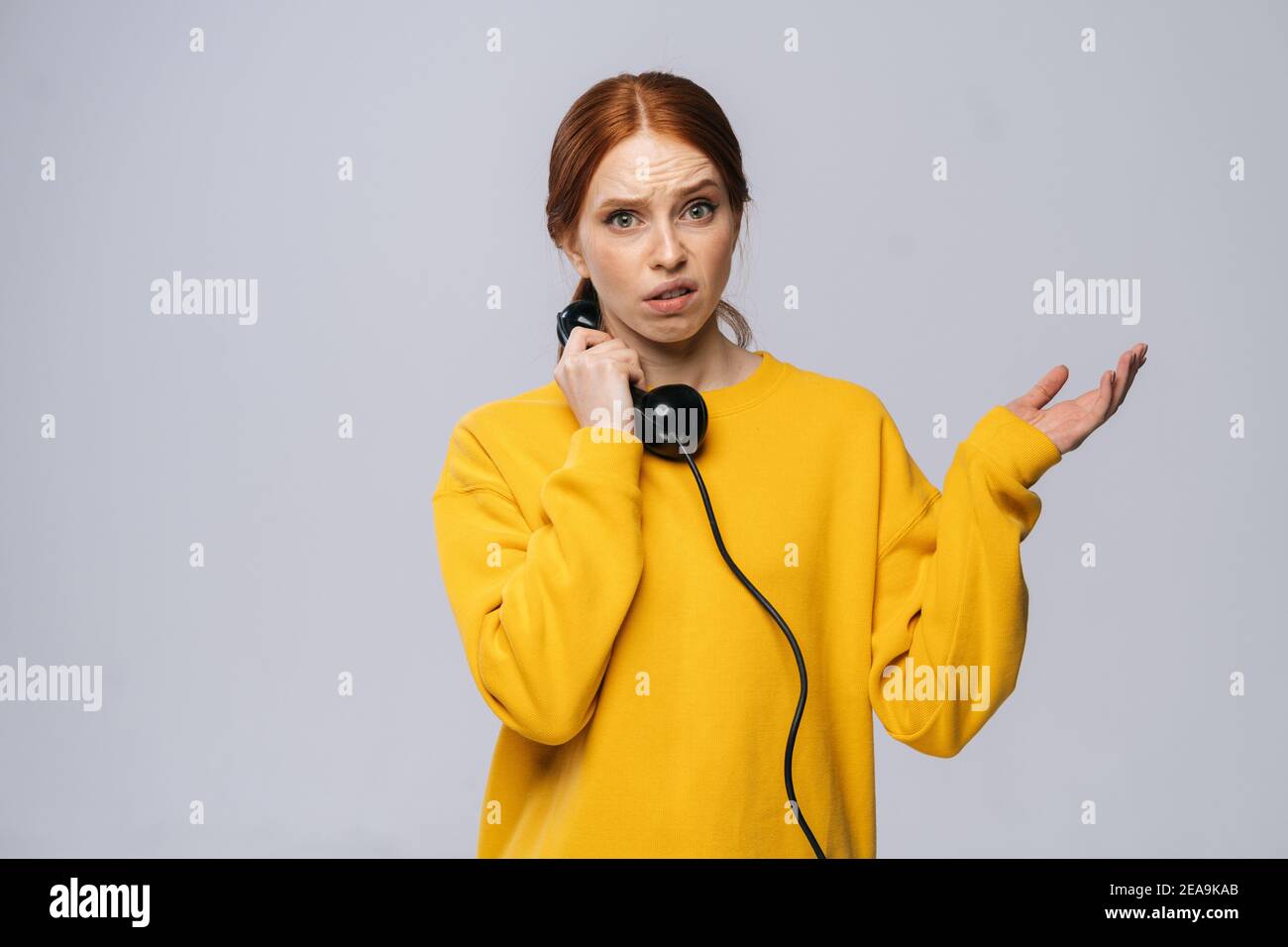 Displeased sad young woman in stylish yellow sweater talking on retro phone and looking at camera Stock Photo