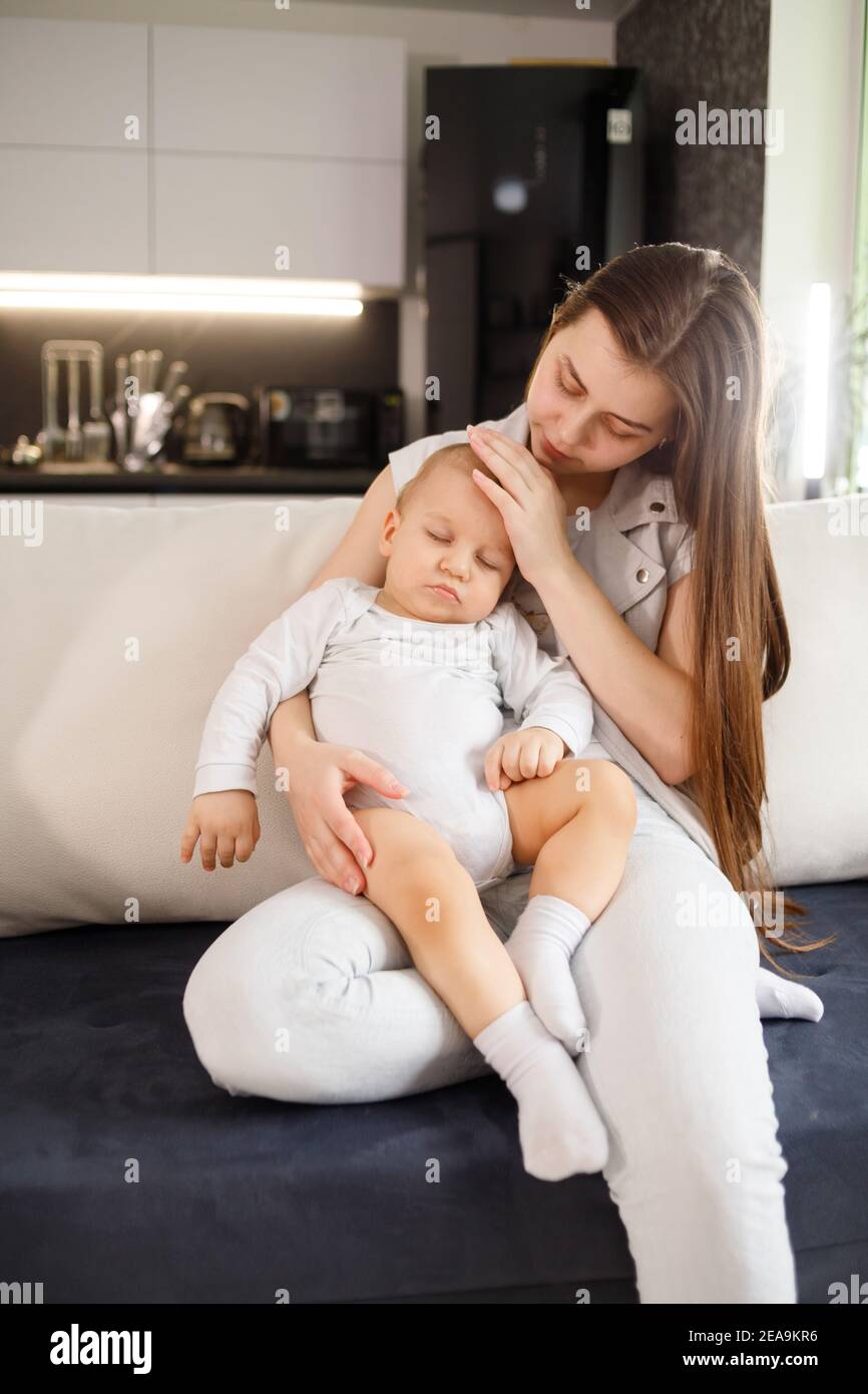 Young mother with sleeping baby on hands on couch at home Stock Photo