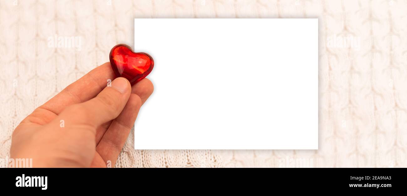 Blank A5 mockup Valentine's Day theme with red heart in hand of boy, knitted sweater background, greeting card and banner photo Stock Photo