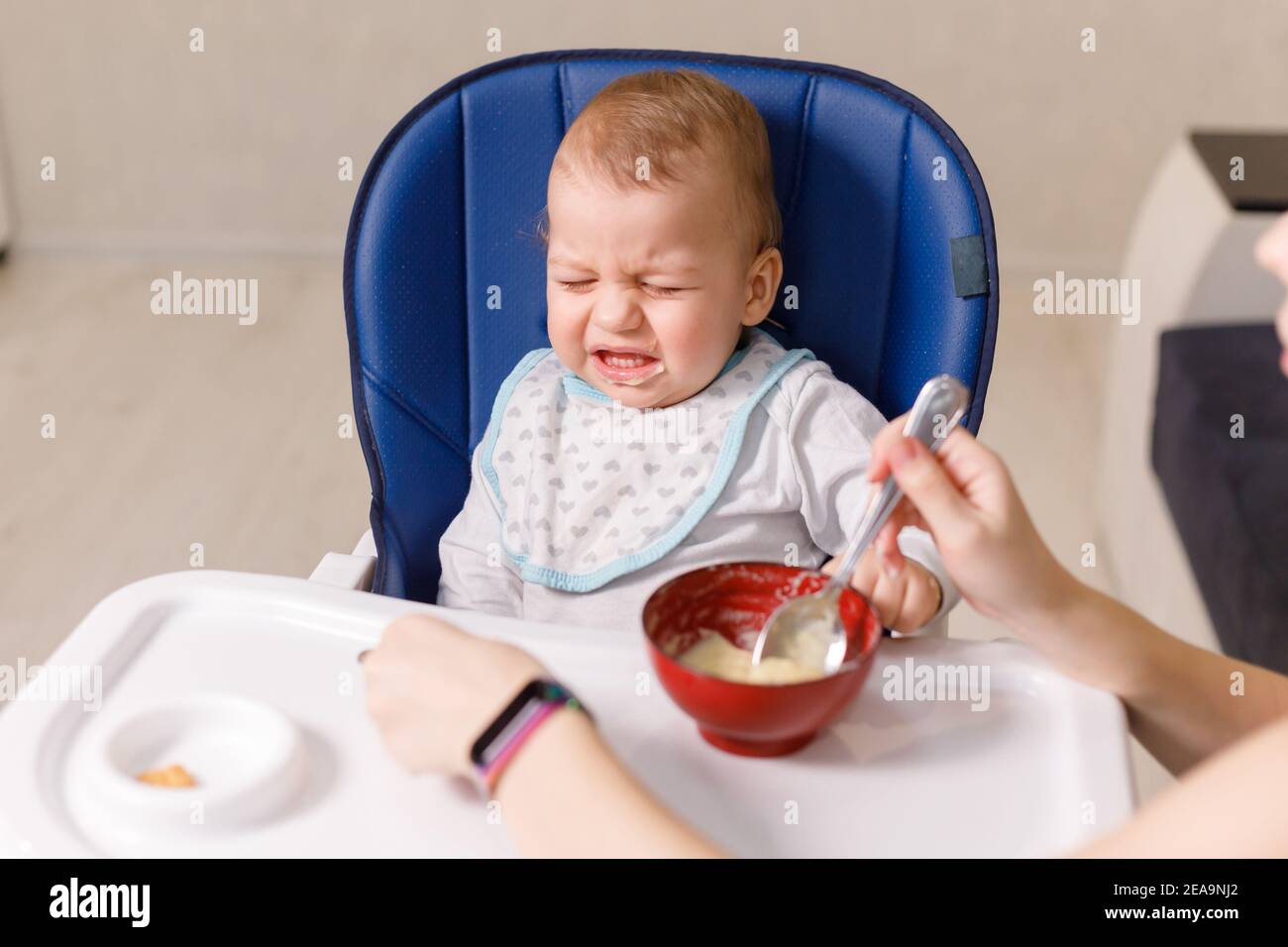 Mother tries to feed with spoon naughty infant kid refusing eating Stock Photo