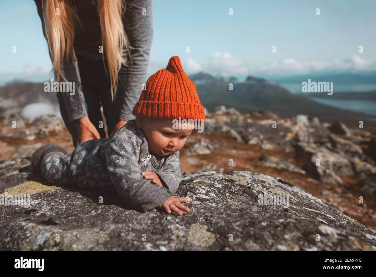 Baby learning crawling outdoor family vacation mother with child infant  wearing orange hat autumn season in Norway Stock Photo