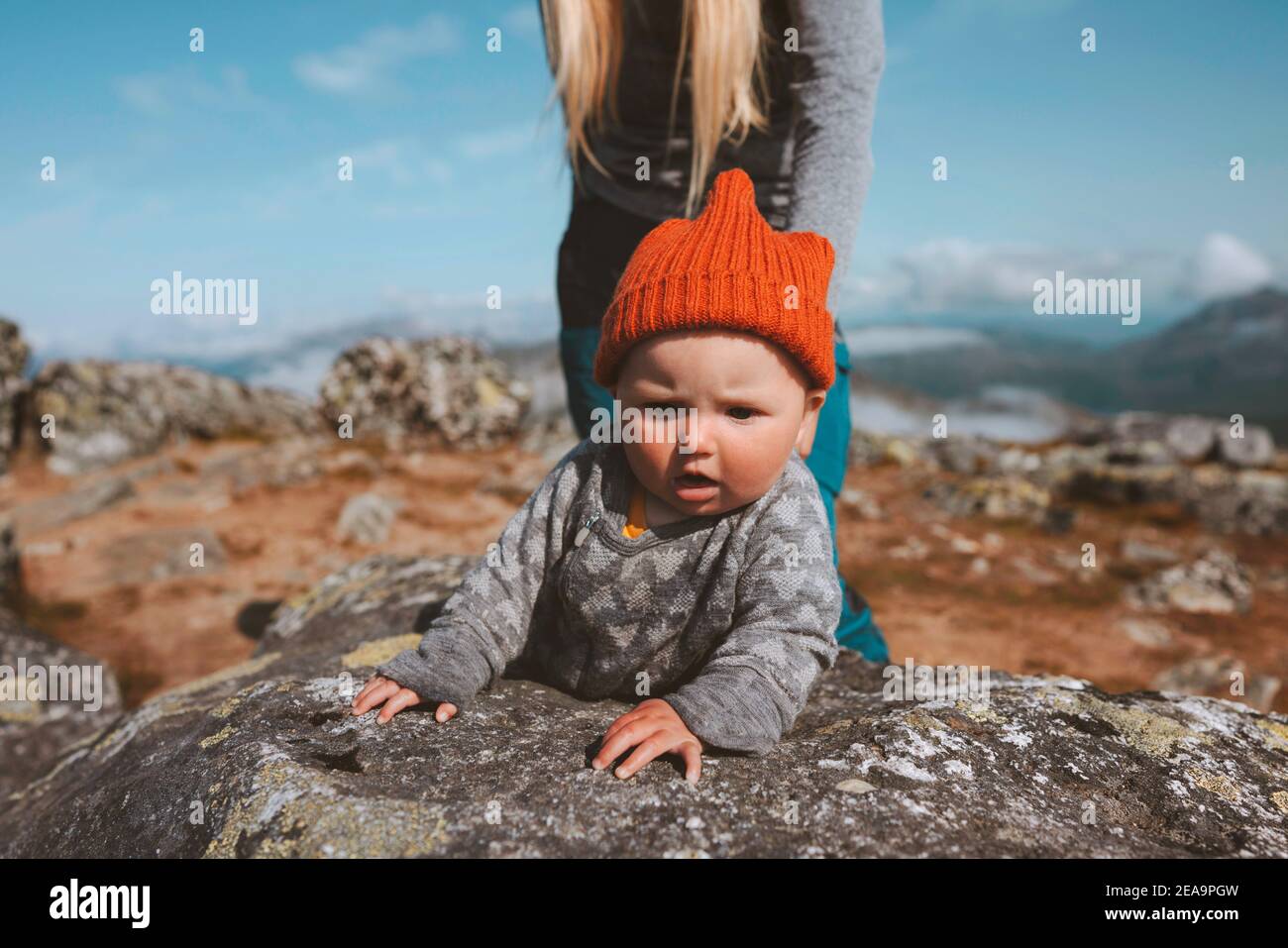 Baby traveler crawling outdoor family lifestyle vacation activity infant child wearing orange hat autumn season trip in Norway Stock Photo