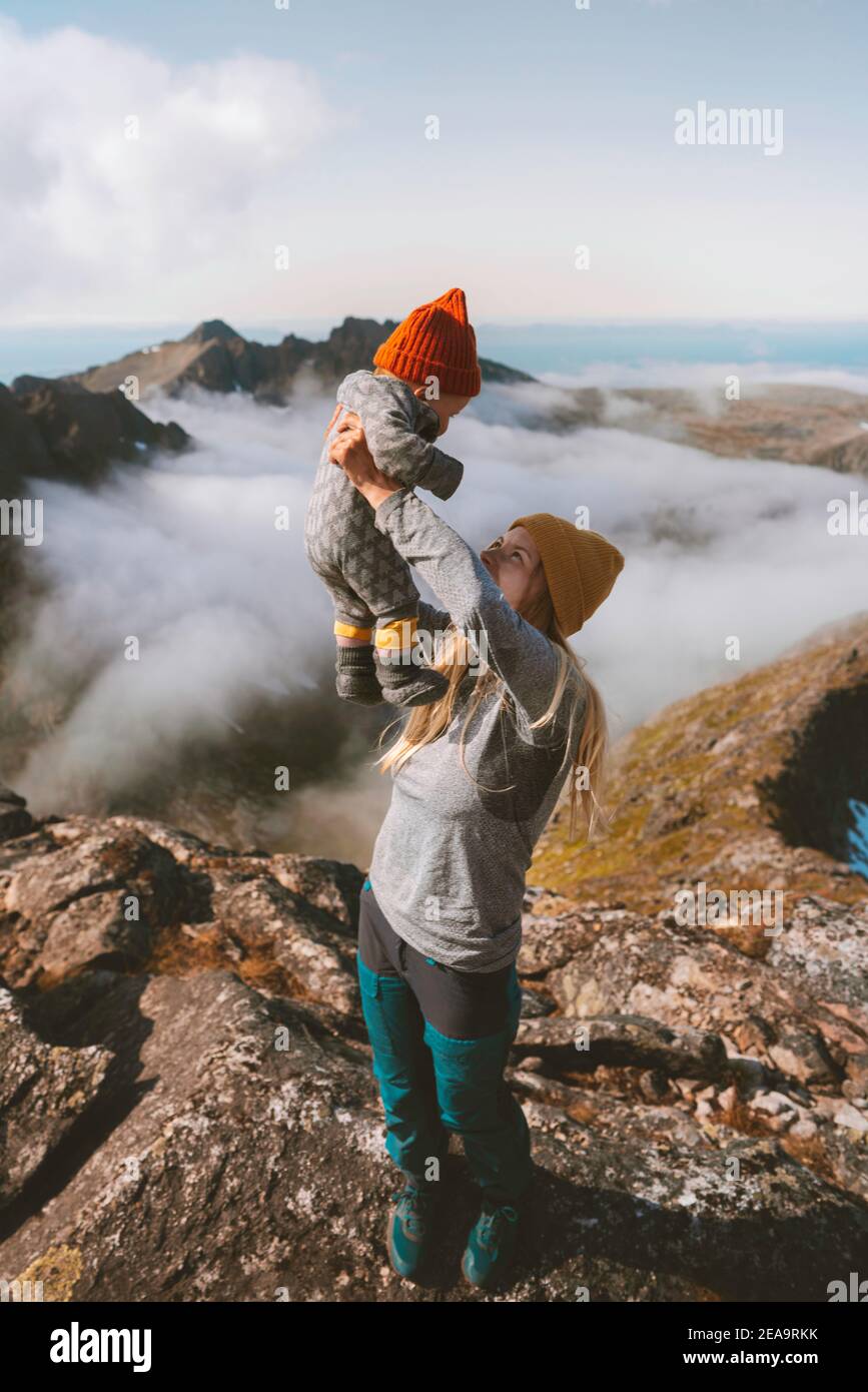 Family travel mother hiking holding up child on mountain summit active vacations outdoor woman playing with baby healthy lifestyle in Norway happy emo Stock Photo