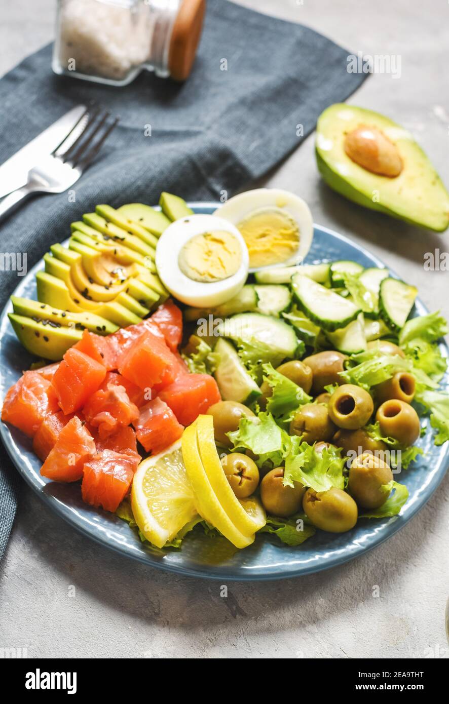 Ketogenic, paleo diet lunch bowl with salted salmon fish, lemon, avocado, olives, boiled egg, cucumber, green lettuce salad, healthy food trend Stock Photo