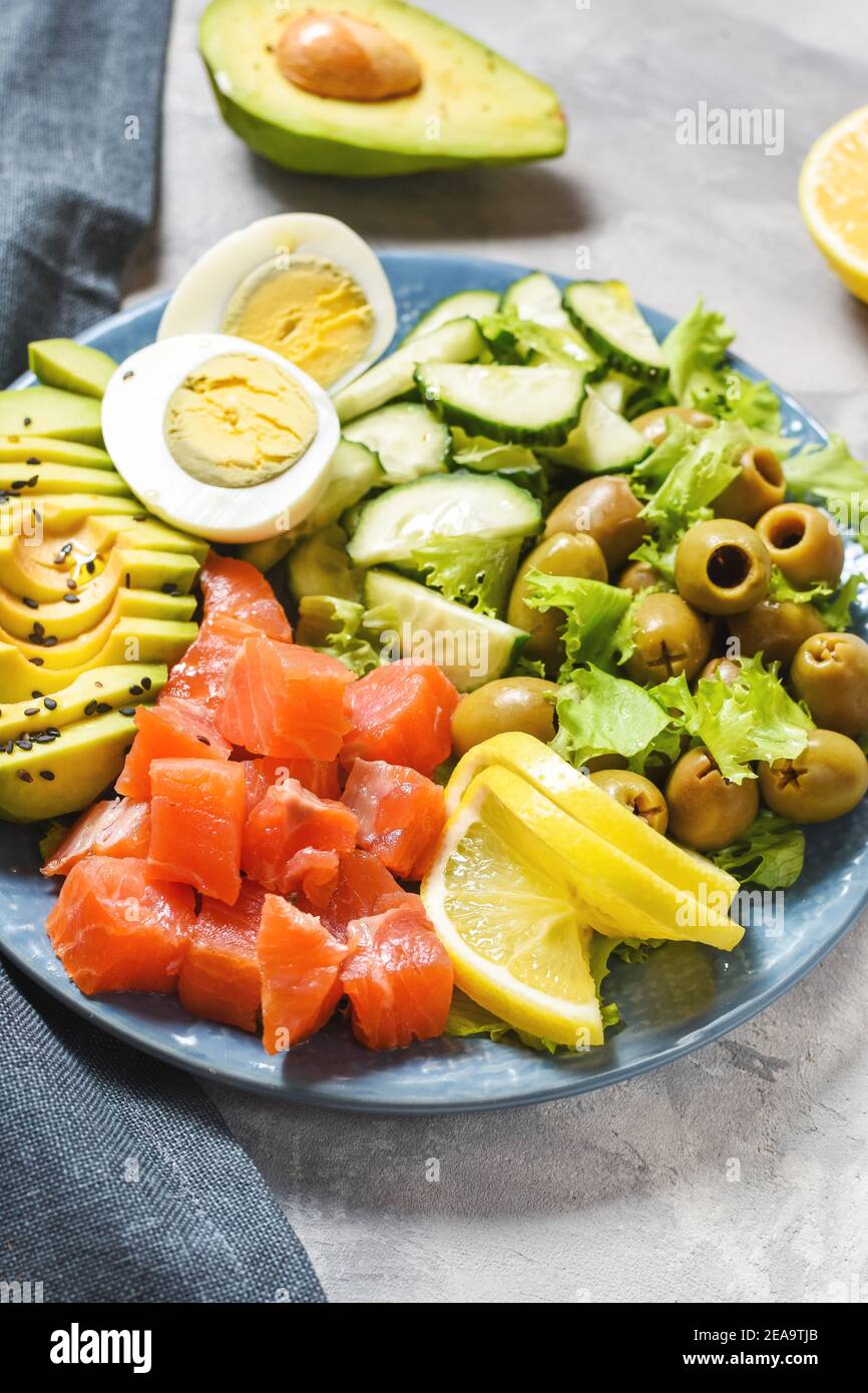 Ketogenic, paleo diet lunch bowl with salted salmon fish, lemon, avocado, olives, boiled egg, cucumber, green lettuce salad, healthy food trend Stock Photo