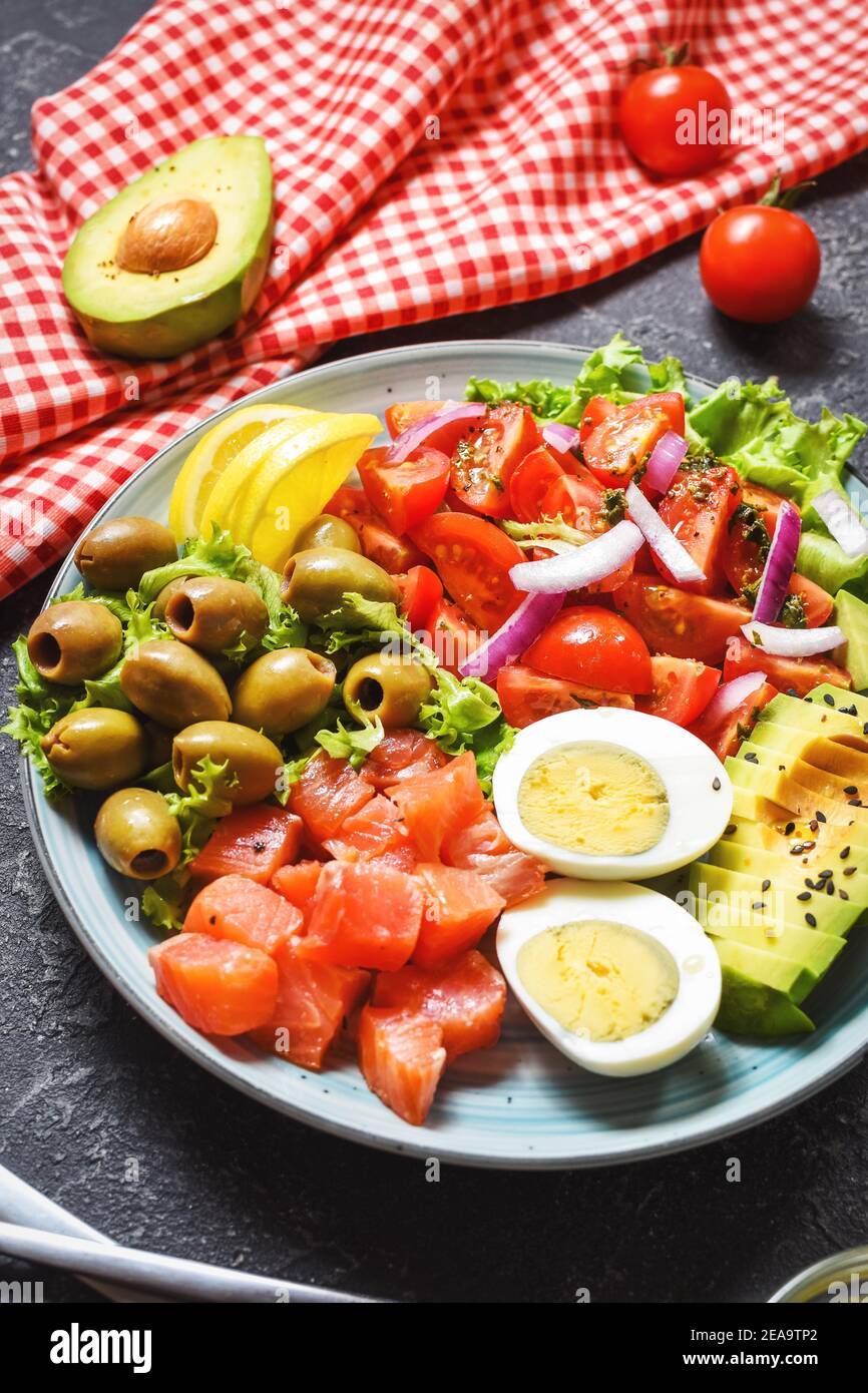 Ketogenic, paleo diet lunch bowl with salted salmon fish, lemon, avocado, olives, boiled egg, tomato, green lettuce salad, healthy food trend Stock Photo