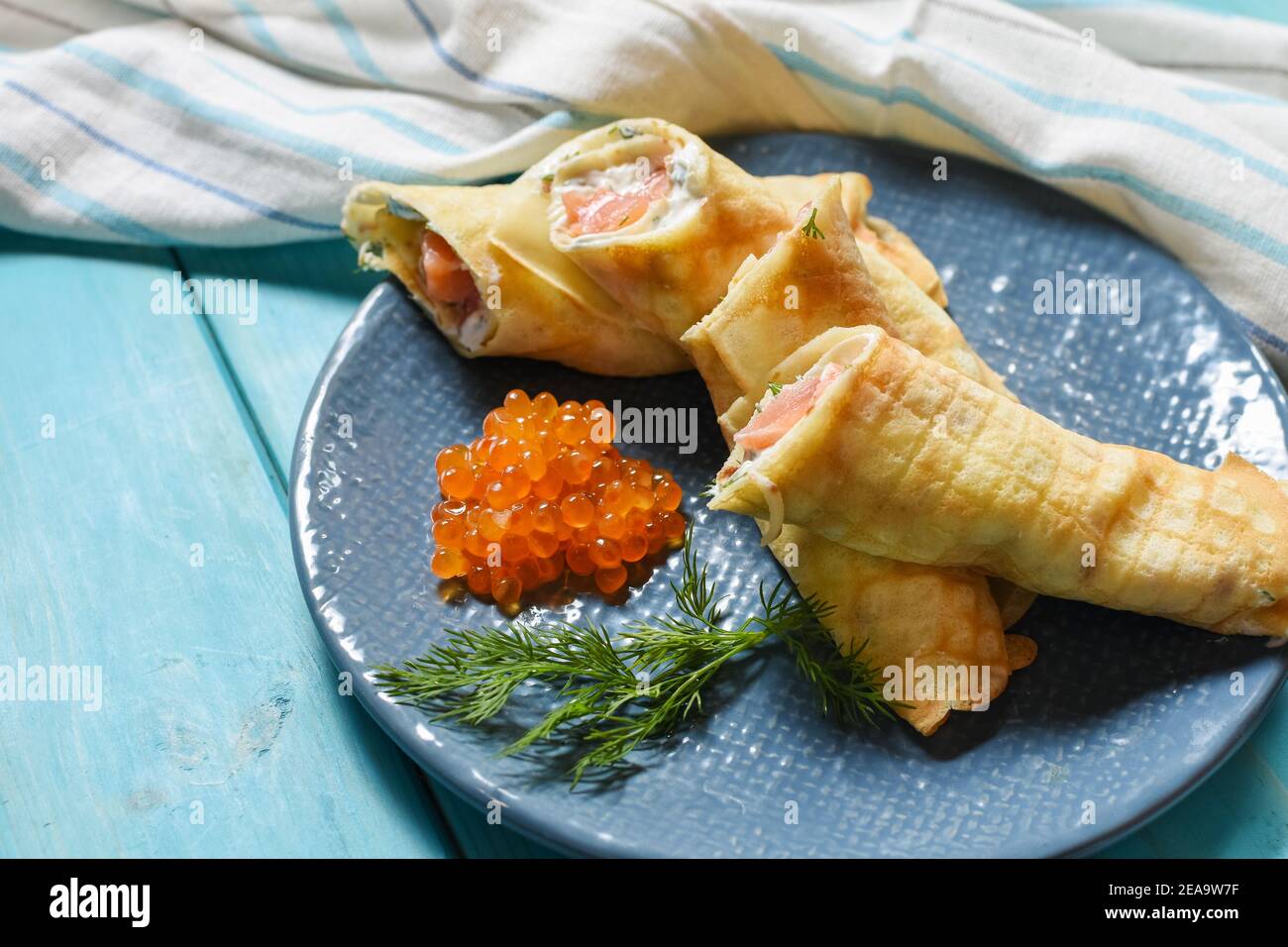 Delicious breakfast - crepes with smoked salmon, sour cream and caviarch on blue wooden background. Stock Photo