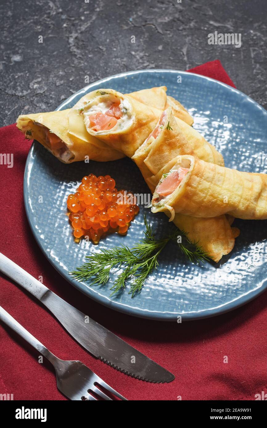 Delicious breakfast - crepes with smoked salmon, sour cream and caviarch on black stone background. Stock Photo