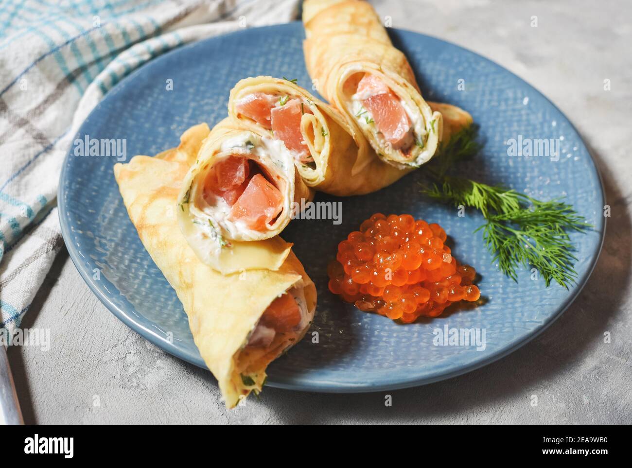 Delicious breakfast - crepes with smoked salmon, sour cream and caviarch on concrete background. Stock Photo