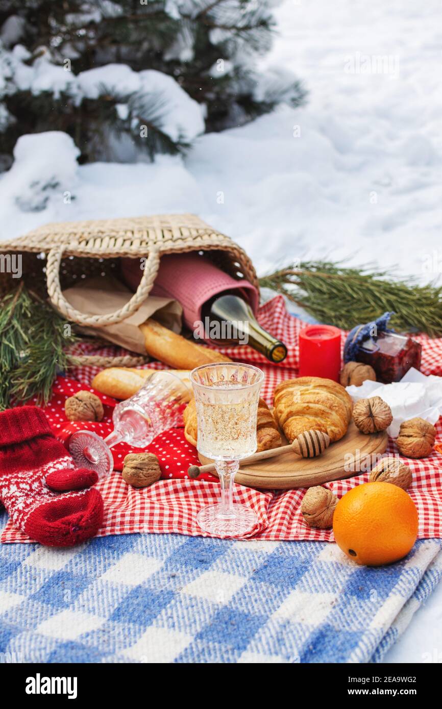 Romantic picnic setting in winter park, color blanket. Fresh food, cheese, oranges, croissants, wine and walnuts. Outdoor relaxing, fresh air eating Stock Photo