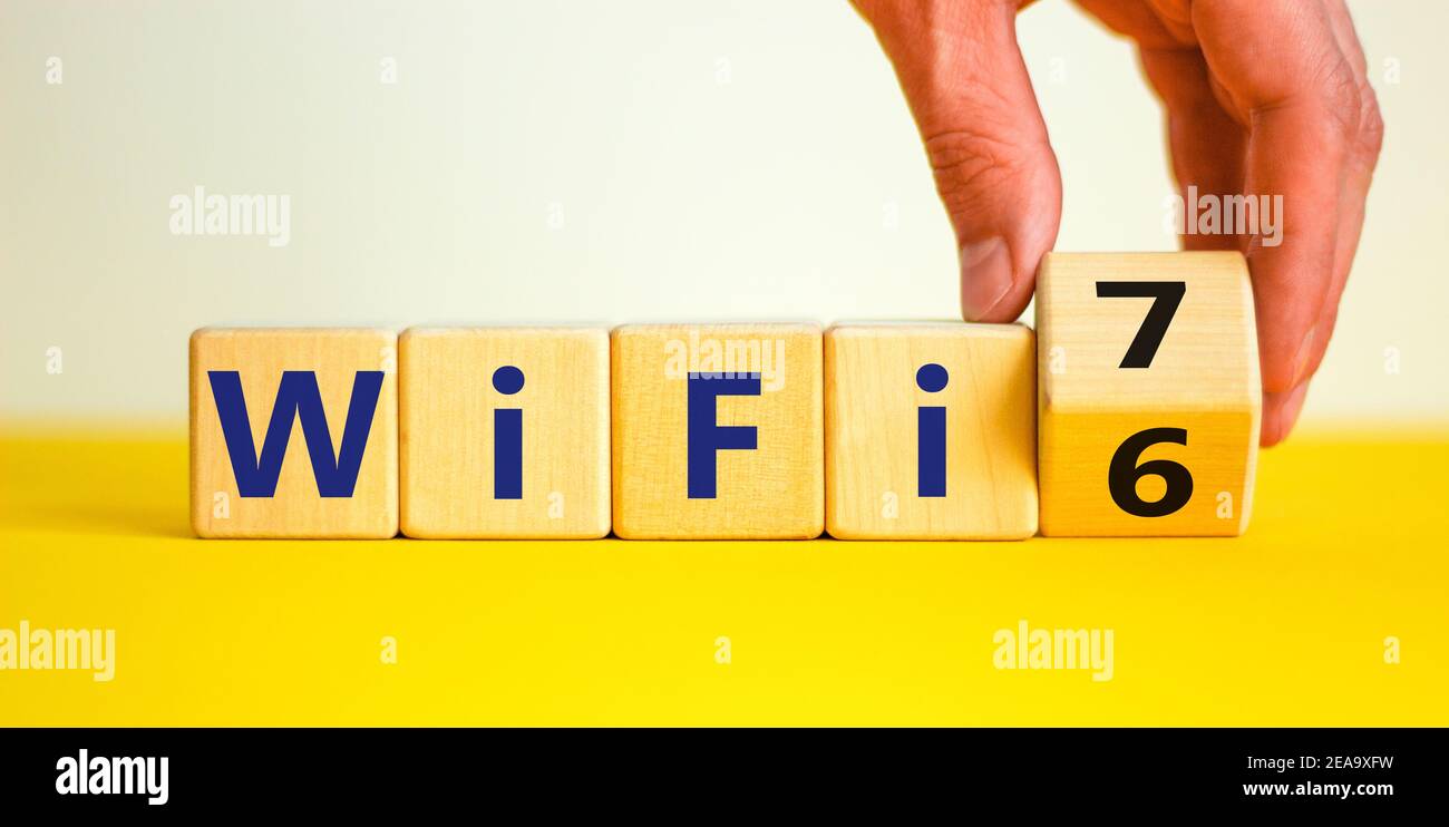 WiFi 6 or 7 symbol. Businessman turns a wooden cube and changes the words WiFi 6 to WiFi 7. Beautiful yellow, white background, copy space. Business, Stock Photo