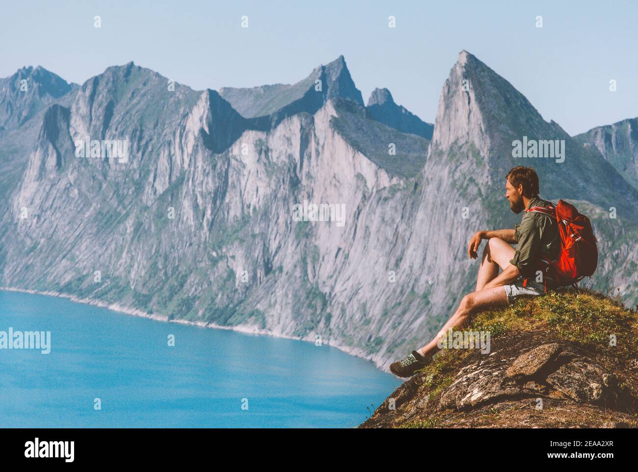 Man relaxing on cliff travel with backpack in Norway hiker enjoying mountains and fjord view adventure vacation outdoor active healthy lifestyle harmo Stock Photo