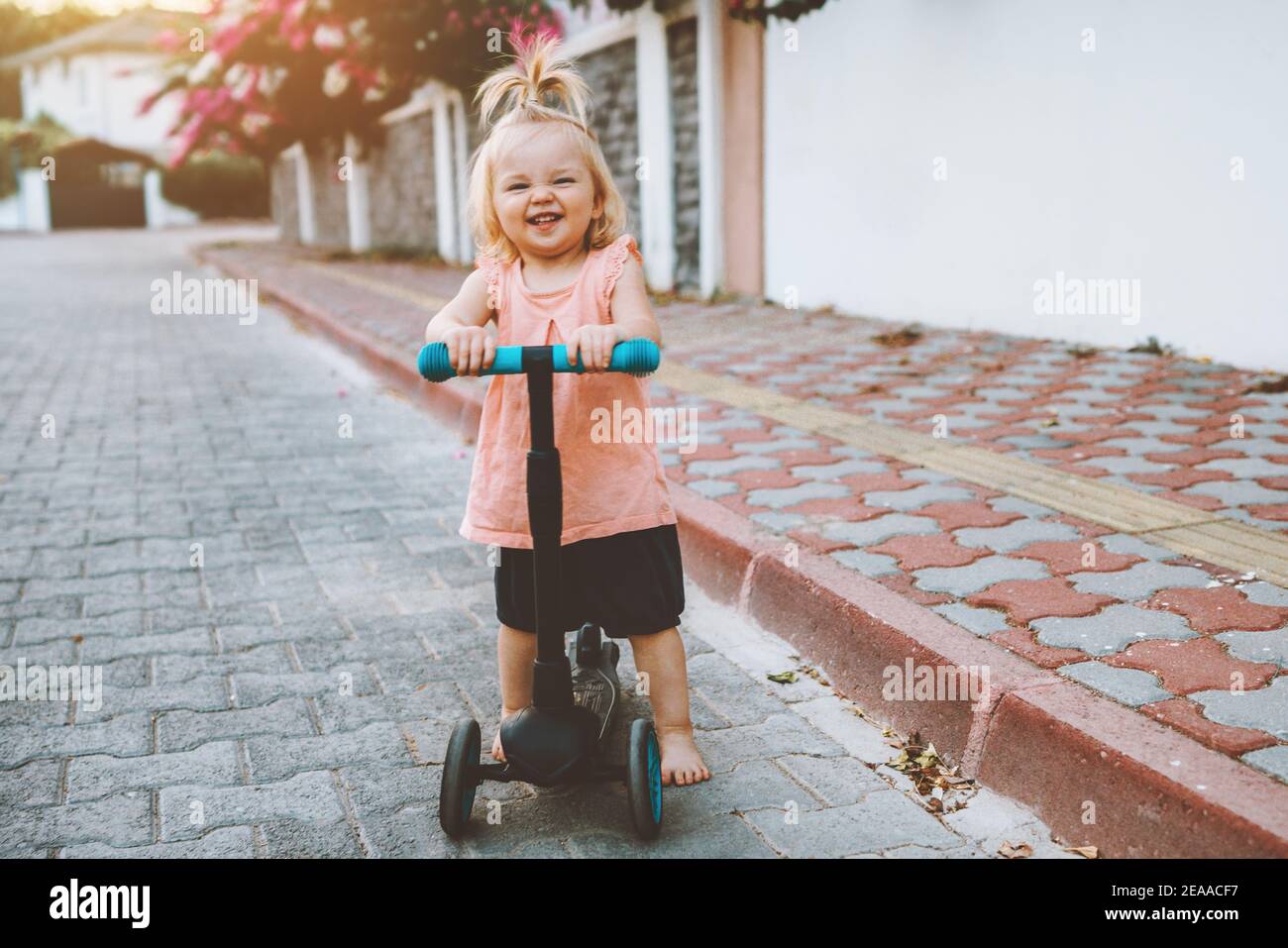 Child girl riding scooter on city street happy baby 1 year old healthy active lifestyle family fun outdoor Stock Photo