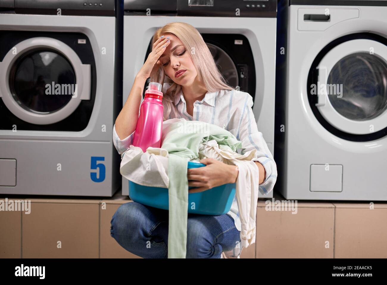woman doing laundry, looking sad and depressed expression, having bad mood after hard working day, in washing house. tired and exhausted staff Stock Photo