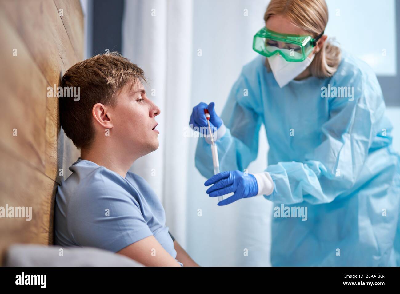 health professional in PPE suit introducing a nasal and throat swab to ...