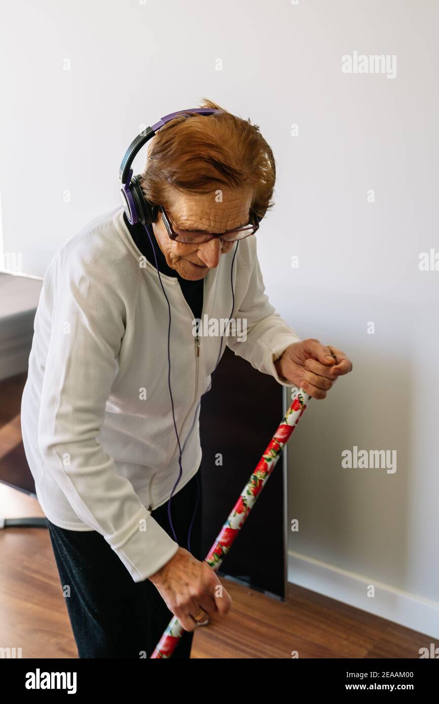 Senior woman listening to music while sweeping and doing household
