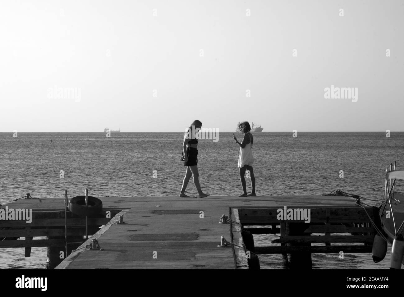 two young women standing at end of jetty grand anse beach grenada windward islands west indies Stock Photo