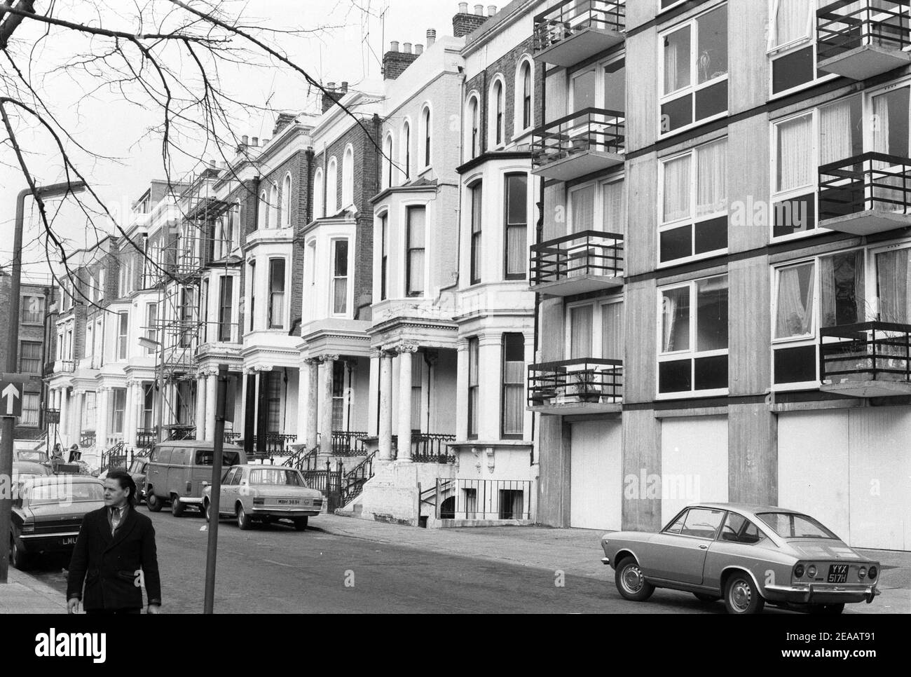 UK, West London, Notting Hill, 1973. Rundown & dilapidated large four-story houses are starting to be restored and redecorated. Near No.2 Powis Gardens. Talbot Tabernacle side entrance sign at the far end of the road by No.9 & 10. To the right are garages of the modern flats of Powis Court. Stock Photo