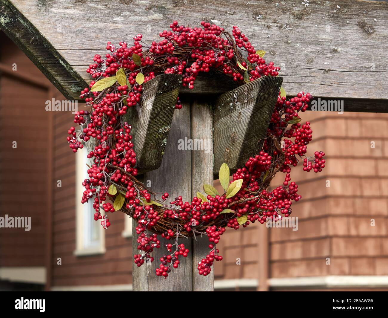 Outdoor holiday red berry wreath with rustic wooden house in background Stock Photo