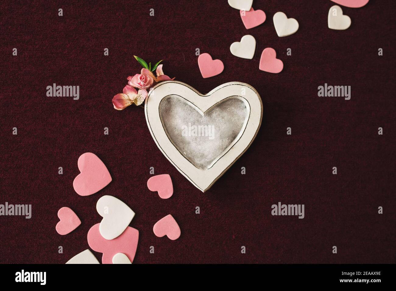 Valentines day newborn photography background - white heart shaped bowl with white, pink and red hearts on burgundy backdrop. Stock Photo