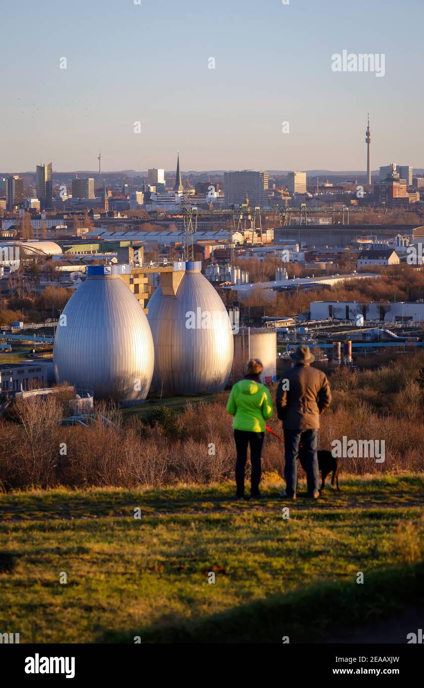Dortmund, Ruhr area, North Rhine-Westphalia, Germany - city panorama of Dortmund, walkers on the Deusenberg in front of the skyline of the Dortmund city center, in the back the Florian and Dortmunder U television tower, in front the digestion towers of the Emscher sewage treatment plant Dortmund Deusen, the sewage treatment plant is now receiving a 4th purification stage, which cleaned it Wastewater also freed from drug residues. Stock Photo