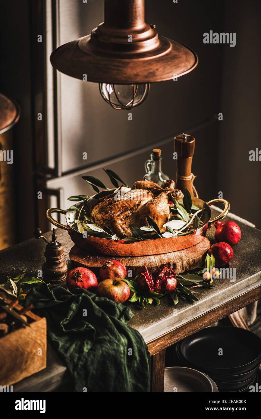 Whole roasted chicken for winter holiday festive dinner in copper roasting tin with spices, herbs and fresh fruit on concrete kitchen counter. Christmas or Thanksgiving Day cooking concept Stock Photo