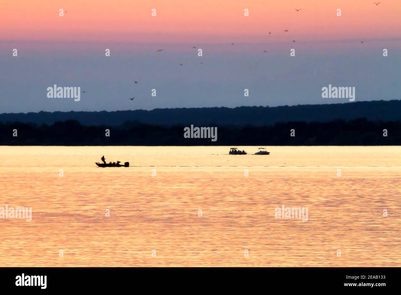 Grand Lake O' the Cherokees at Grove Oklahoma is well loved by fishermen as depicted in this photo of three boats on the water at sunset. Stock Photo