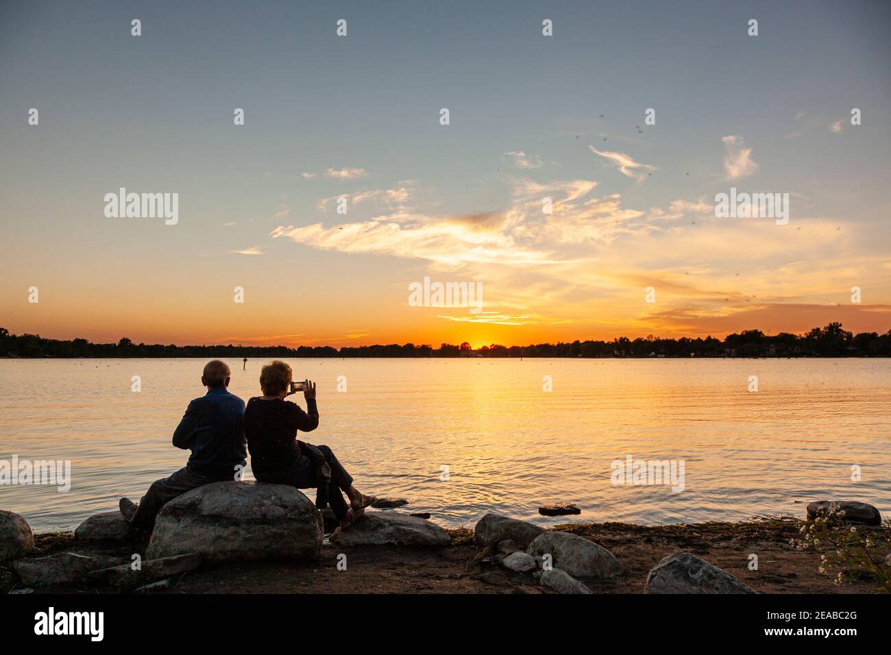 Senior couple silhouetted against a gorgeous sunset on a lake. Stock Photo