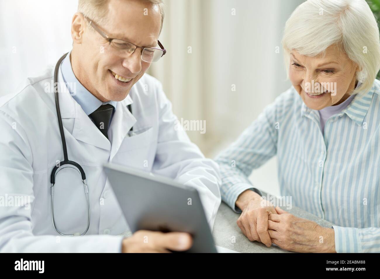 Cheerful doctor using tablet computer while talking with old lady Stock Photo