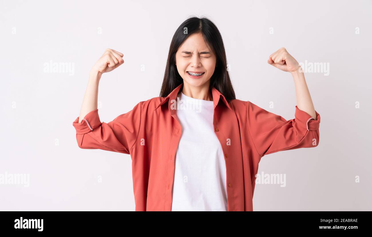 Young Asian woman with braces on teeth in toothy smile and raises arms and shows strong powerful. Stock Photo