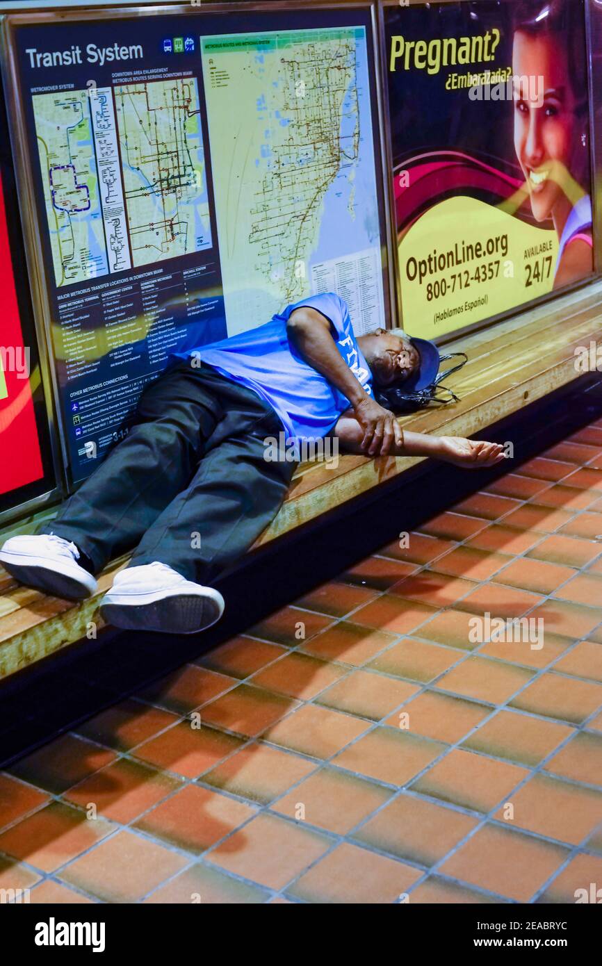 A man sleeps on a bench in the Historic Overtown Metrorail Station in downtown Miami, Florida. Stock Photo