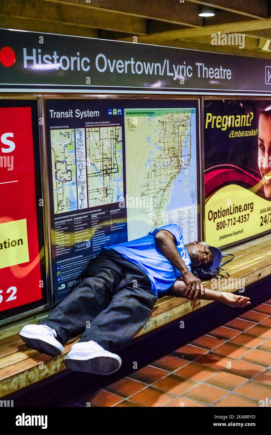 A man sleeps on a bench in the Historic Overtown Metrorail Station in downtown Miami, Florida. Stock Photo