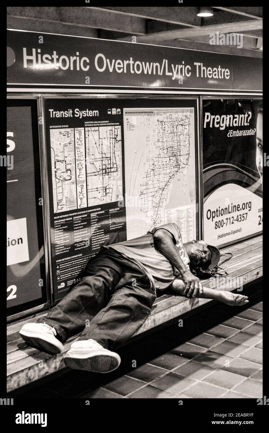 A man sleeps on a bench in the Historic Overtown Metrorail Station in downtown Miami, Florida. Stock Photo