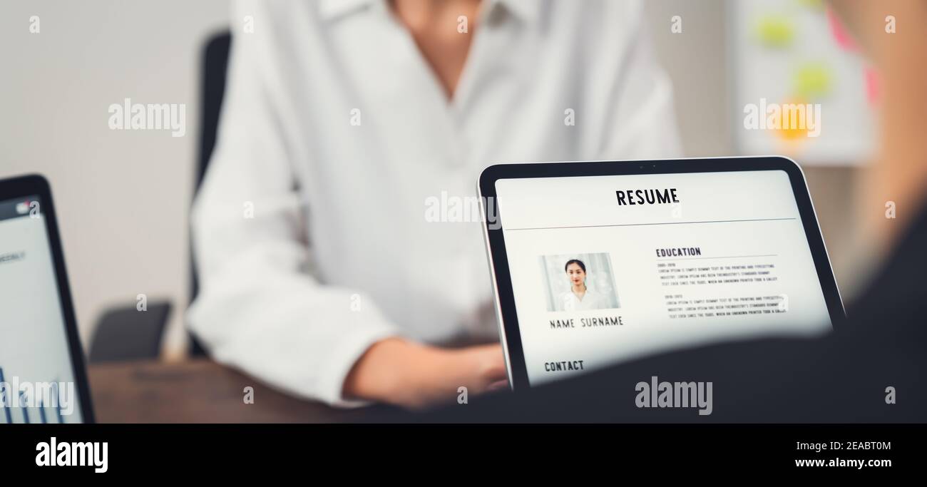 Company Human Resource (HR) is holding a resume application on tablet in hand. Young Asian woman talking to give job interviews. Stock Photo