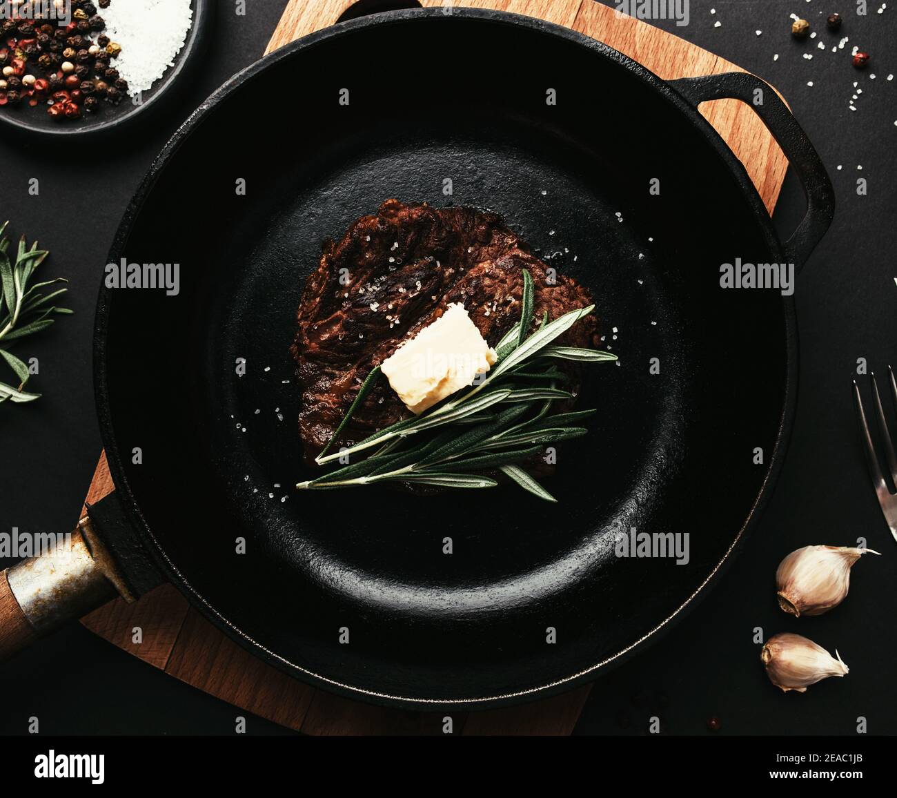 Cooked ribeye steak on castiron pan, rosemary, garlic, knife, fork