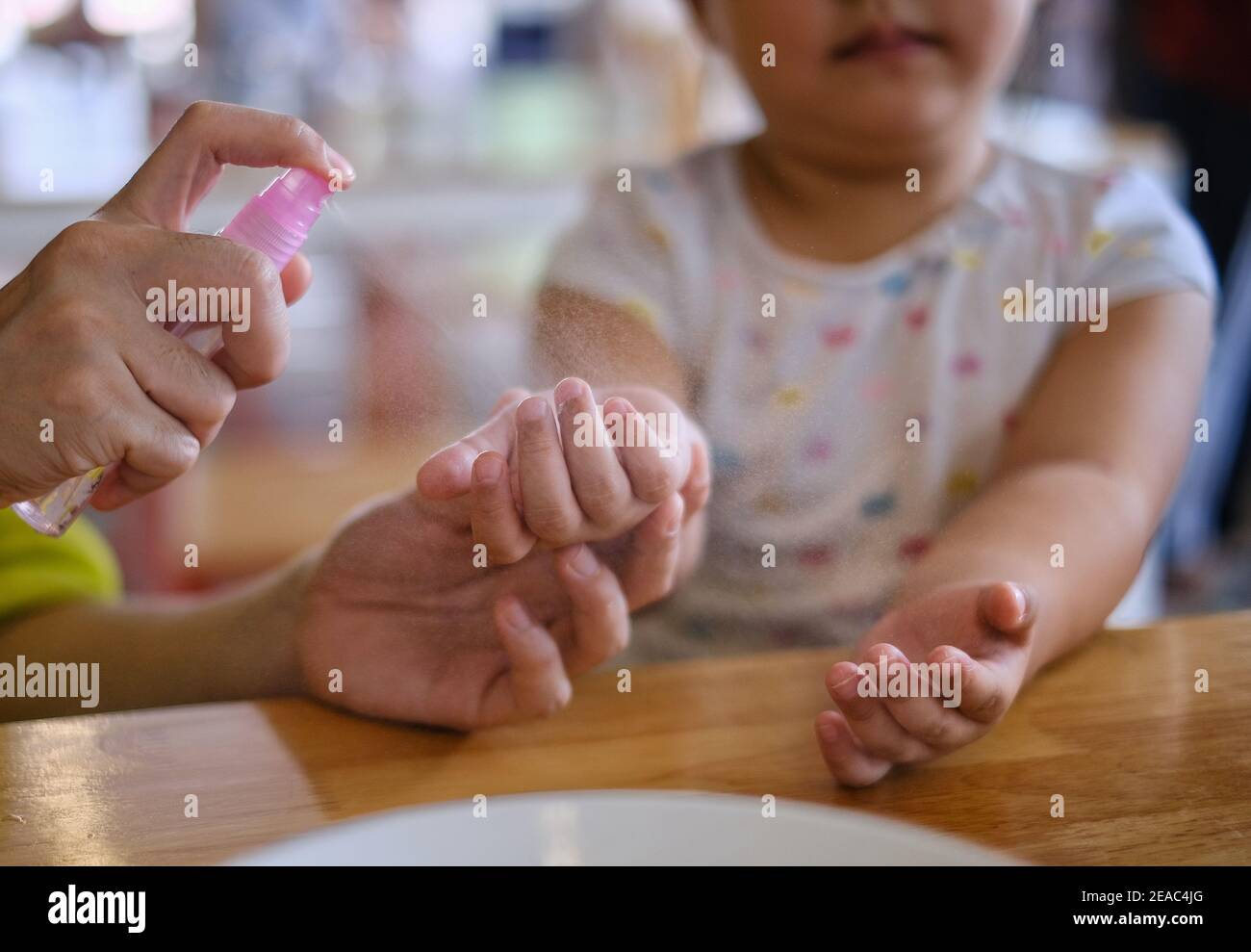 A mother spraying alcohol cleansing spray on her young daughter's hands