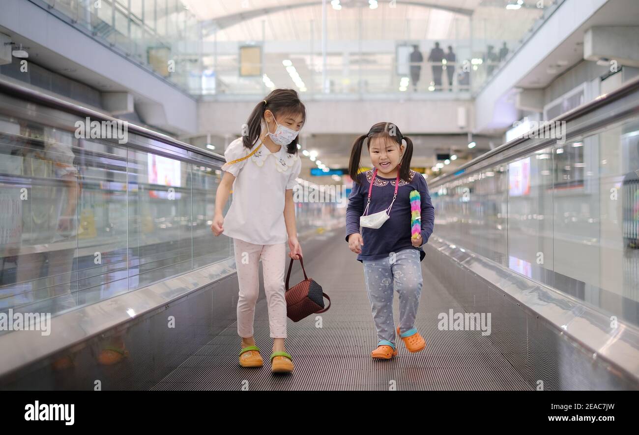 Samut Prakan, Thailand - 11/11/2020: Two sisters playfully walking and jumping around on a moving walkway at a terminal on their way to their gate at Stock Photo