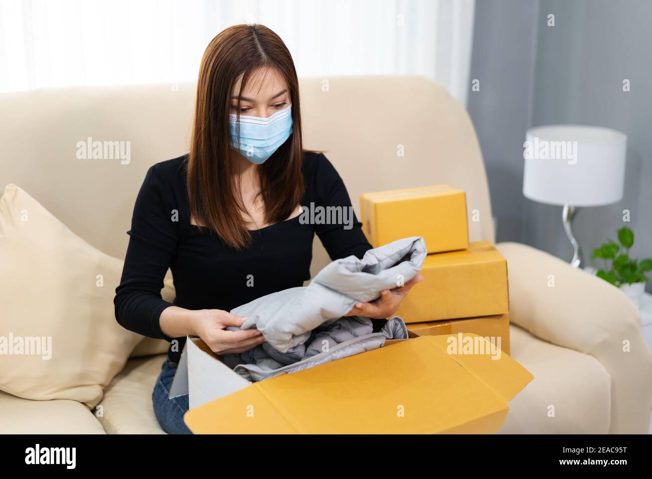 woman with a face mask opening cardboard parcel box at home during the ...