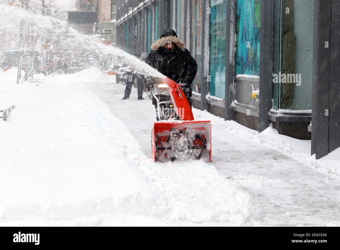 A person uses a snowblower to clear snow from a sidewalk after a winter snowstorm in New York, NY. Stock Photo