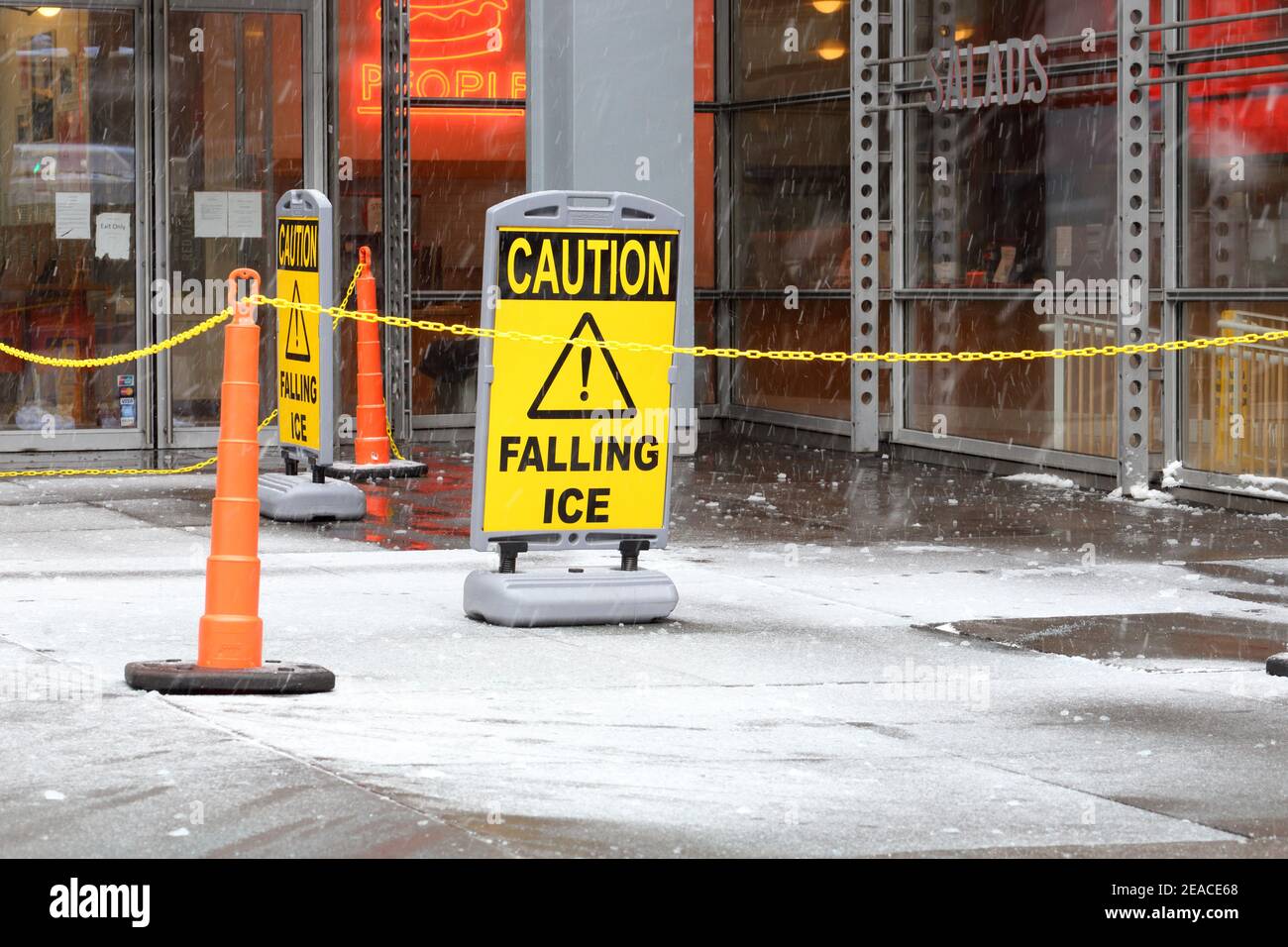 'Caution Falling Ice' signage posted outside a NYC office building with steel and glass curtain wall construction, during freezing winter weather Stock Photo