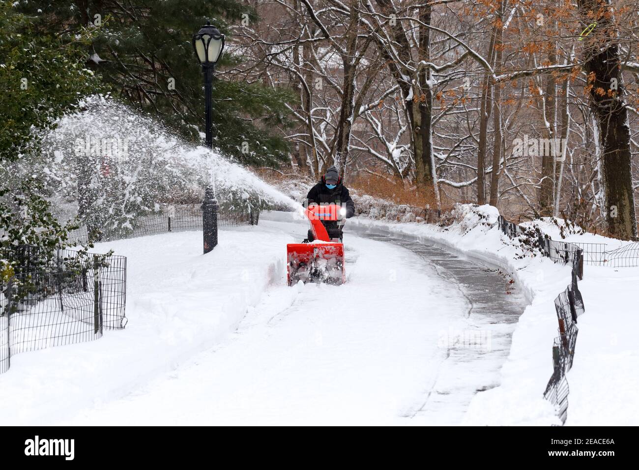 A worker clears snow from a Central Park pathway with a snowblower after a winter snowstorm in New York, NY. Stock Photo