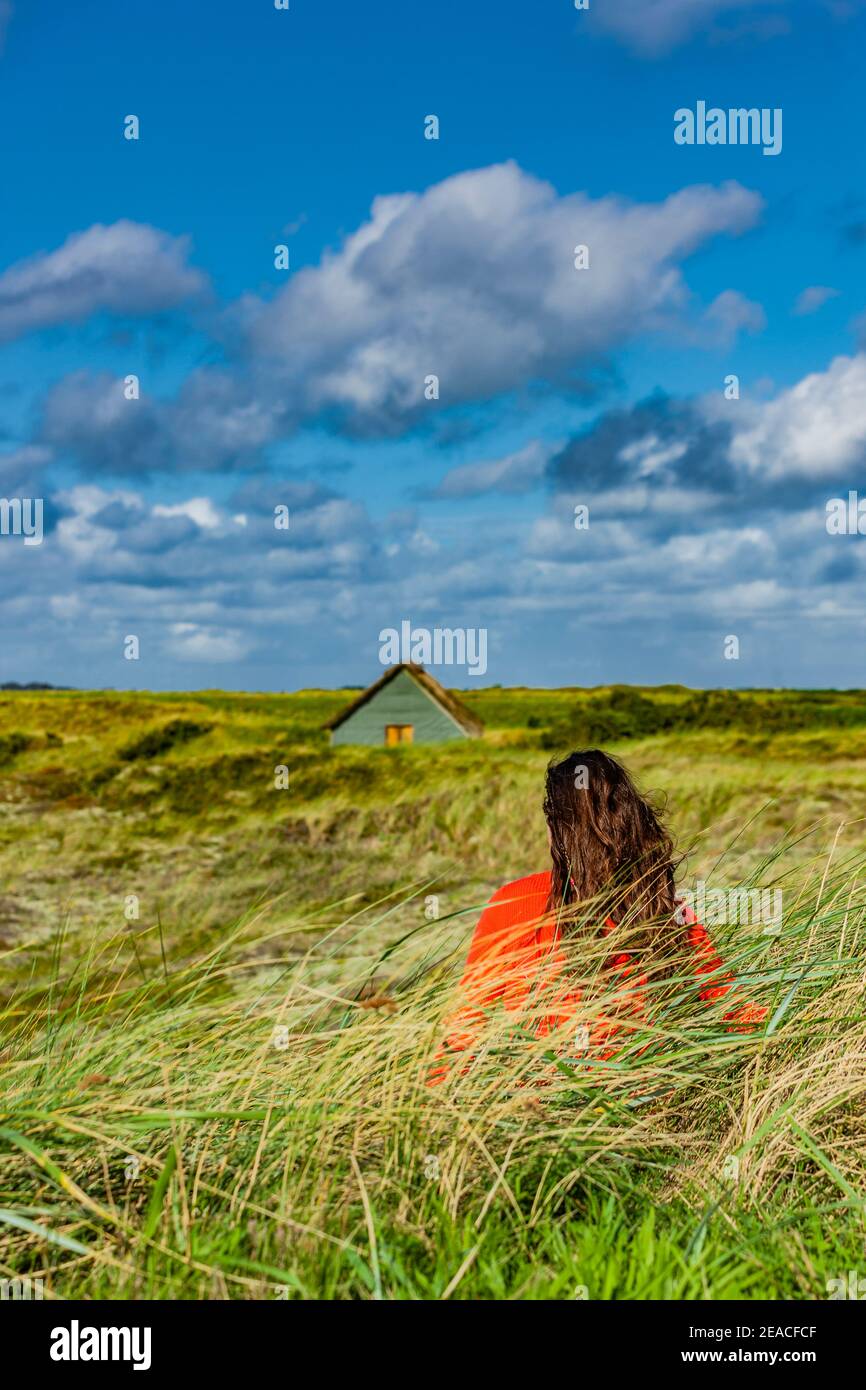 Woman with a red sweater in the dunes in front of a thatched roof house Stock Photo