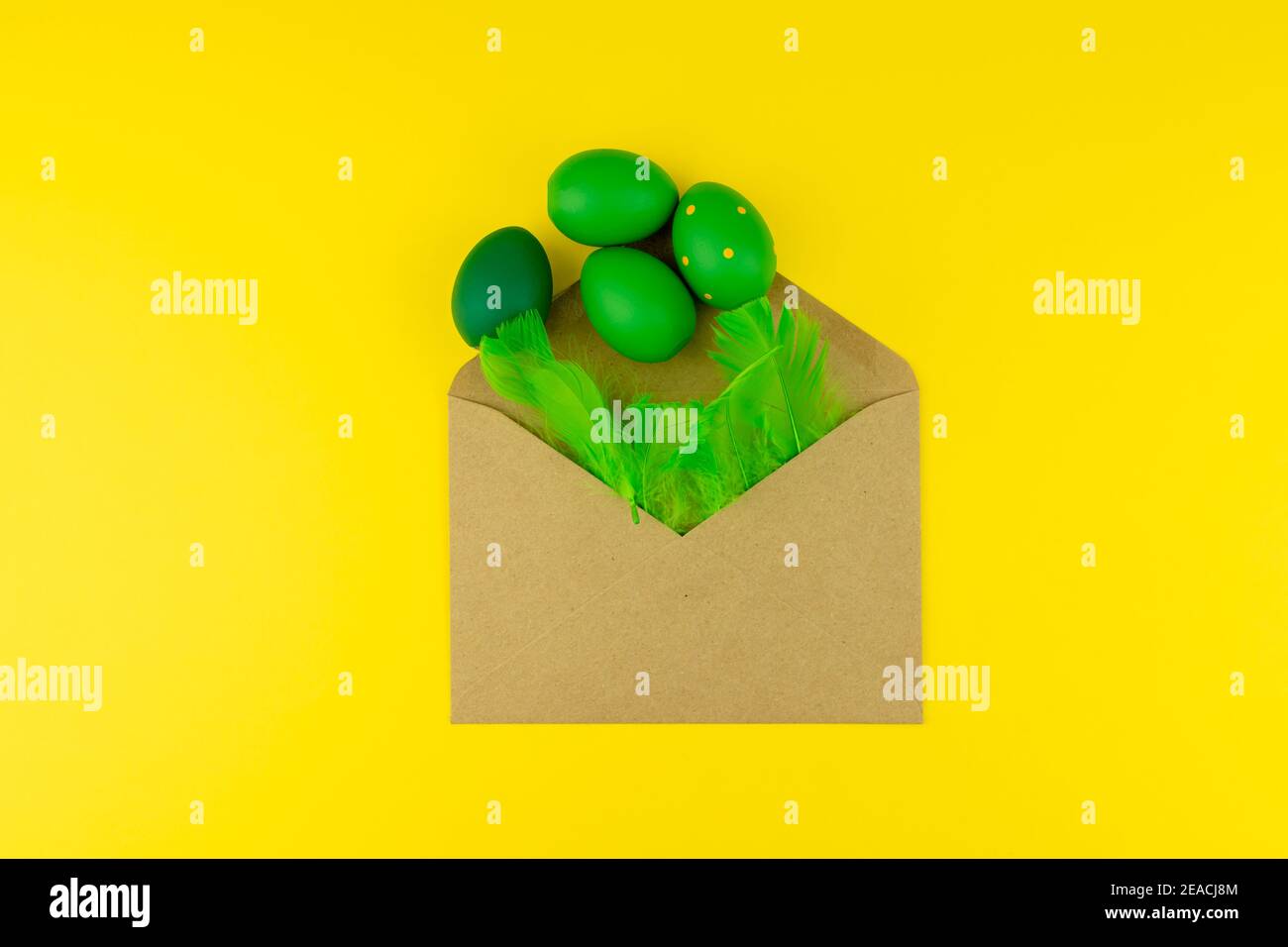 Spring Easter layout with green feathers and eggs, craft envelope on yellow background. Copy space for text for text Stock Photo