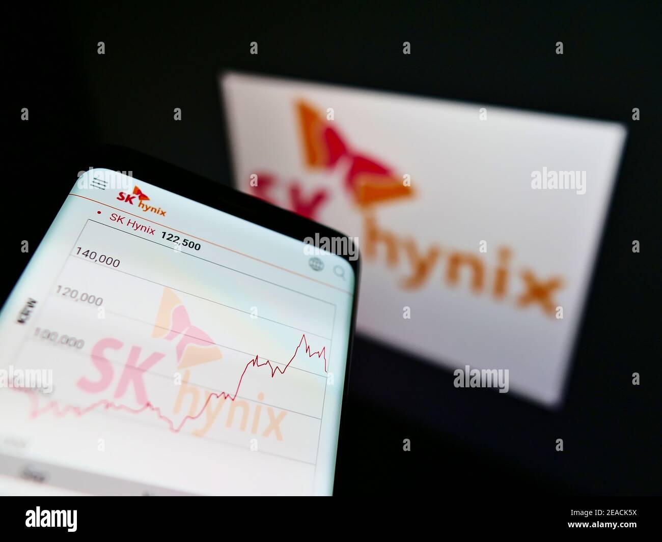 Smartphone with stock price chart of South Korean semiconductor manufacturer SK hynix on screen with logo. Focus on top-center of phone display. Stock Photo