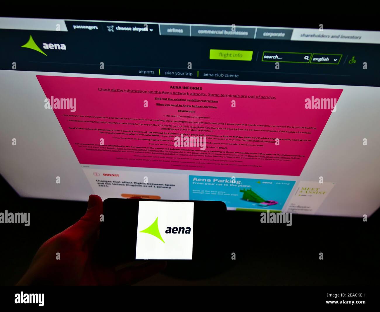 Person holding cellphone with logo of Spanish airport operator Aena S.A. on screen in front of company web page. Focus on smartphone display. Stock Photo