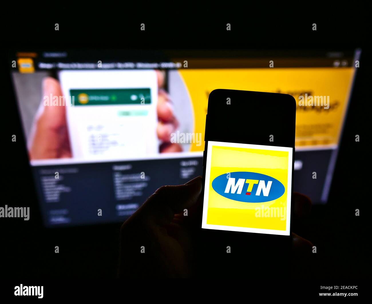 Person holding smartphone with logo of South African telecommunications company MTN Group on screen in front of website. Focus on phone display. Stock Photo