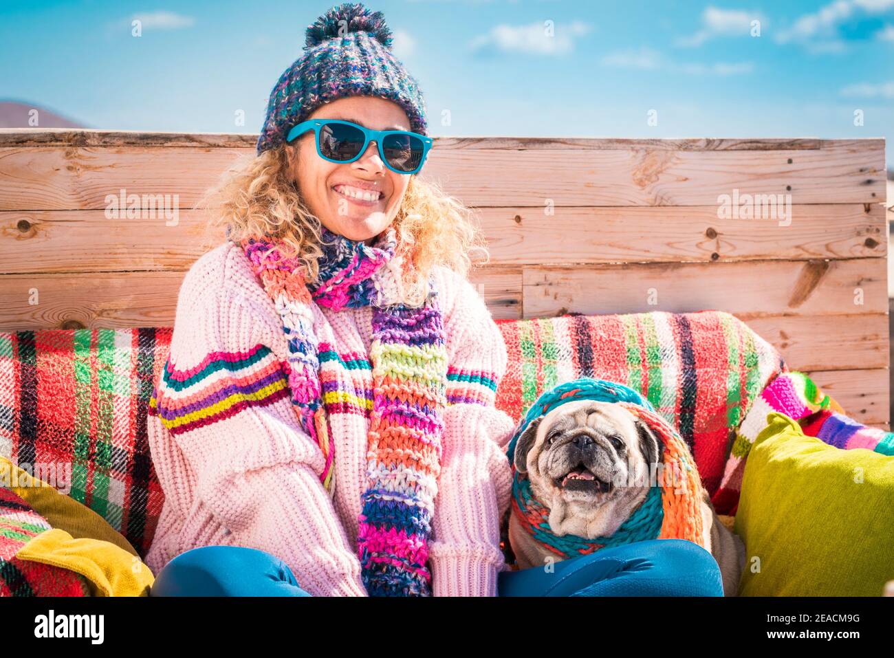 Winter and colorful happy portrait of cheerful beautiful young woman and dog sitting outdoor together - people and animals concept - blue sky in background outdoor activity with animals Stock Photo