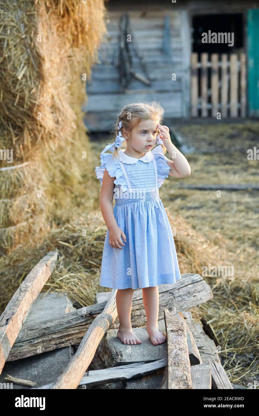 ute little funny girl in a blue dress is splaying in the village yard ...