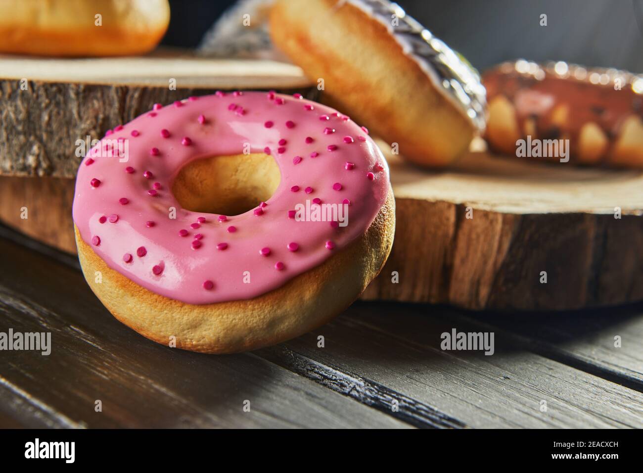 Multicolored donuts with glaze and sprinkles on wooden coasters on a black background. Stock Photo