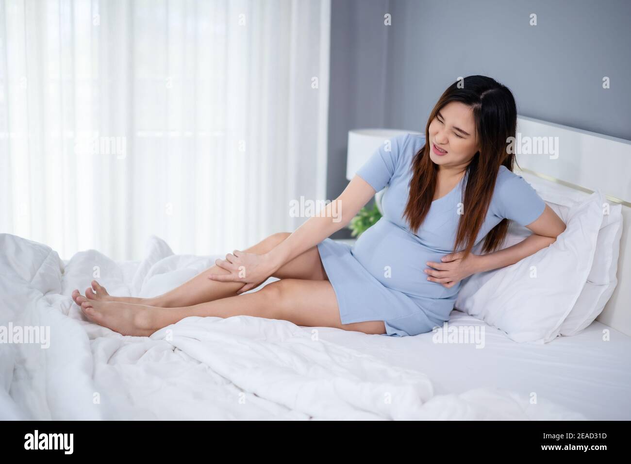 pregnant woman massaging leg on a bed, painful muscle, sprain or cramp